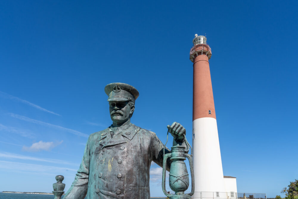 Barnegat Light, Nj Oct. 15, 2020: Bronze Statue Titled "lighthouse Keeper" By Brian Hanlon At The Barnegat Lighthouse State Park With The Lighthouse In The Background.